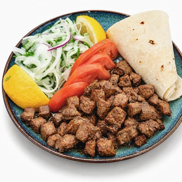 A blue plate with diced meat, sliced tomatoes, onion salad, lemon wedges, and flatbread.
