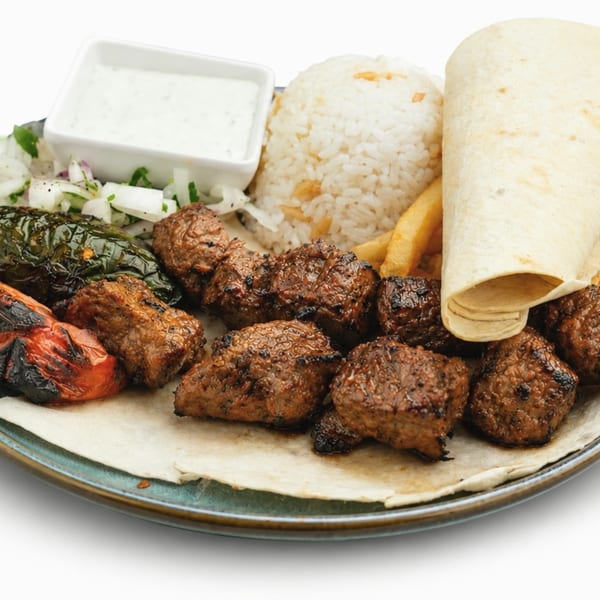 Grilled meat skewers, rice, fries, charred vegetables, and a white sauce on a plate.