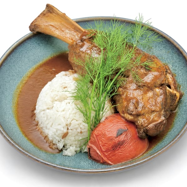 Braised lamb shank with rice, roasted tomato, and fresh dill on a blue plate.